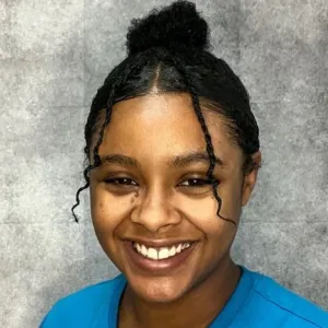 Jasmine has curly black hair and is smiling in front of a grey backdrop